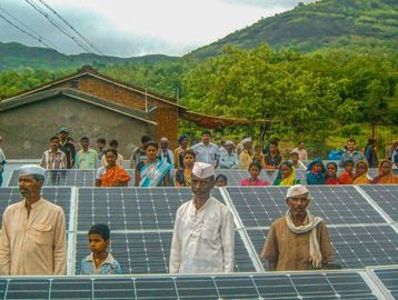 Village people standing near solar panels.