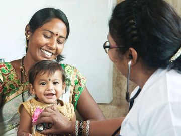A doctor examining a smiling baby held by her mother.