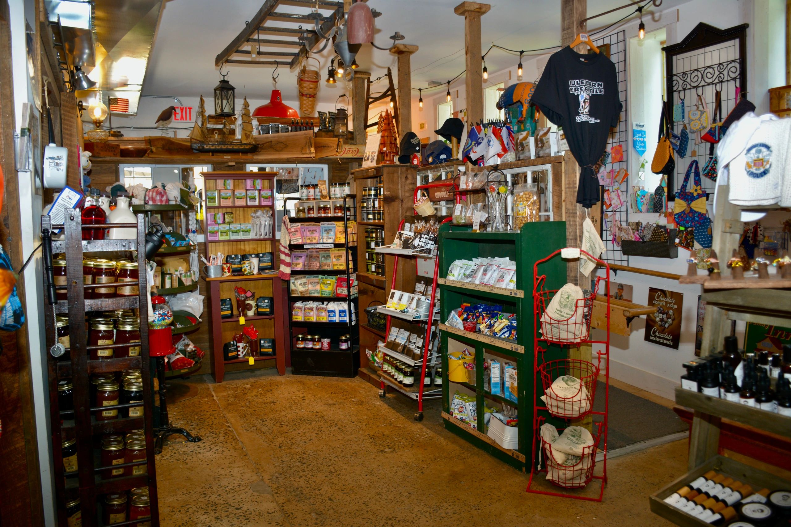 Interior of a rustic general store-style retail incubator featuring shelves stocked with handmade goods, local products, and artisan crafts displayed in a cozy, vintage setting.