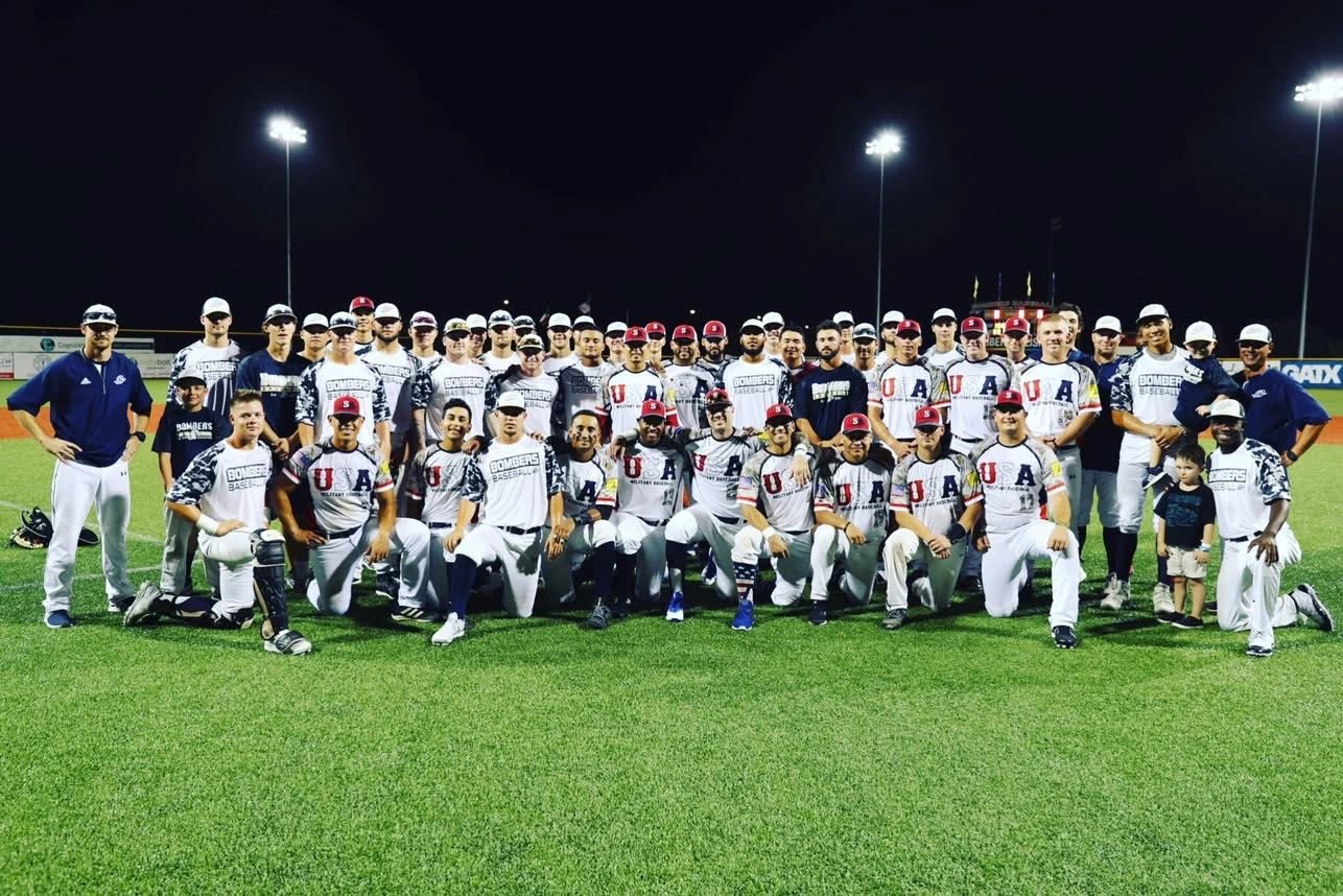 A large group of baseball players and coaches pose on a field at night.
