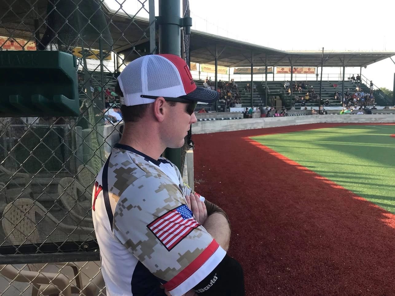 A baseball player in a camouflage jersey watches the game from the dugout.