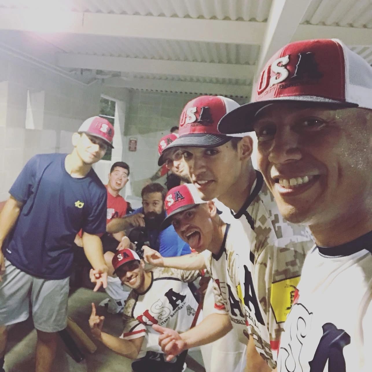 A group of smiling men wearing USA baseball caps and sports jerseys indoors.