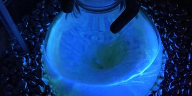 A hand holding a glass flask illuminated by blue light surrounded by shiny beads.