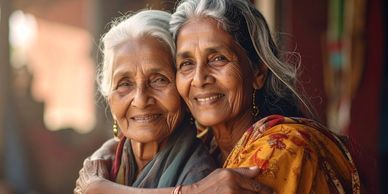 Two elderly women smiling and embracing warmly.