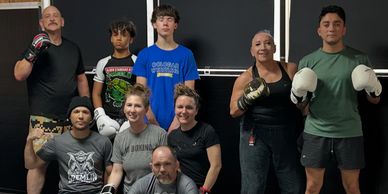 Group of people posing with boxing gloves in a gym setting.