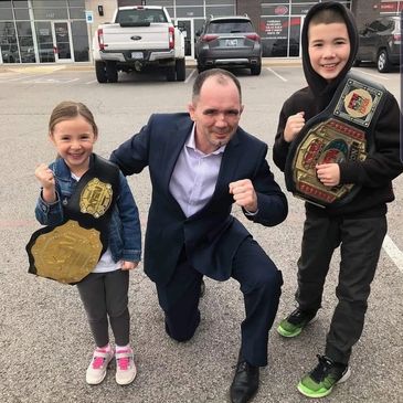 Kids smiling with professor stockton and some of his belts