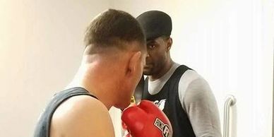 Boxer wearing red gloves faces a trainer in a focused training session.