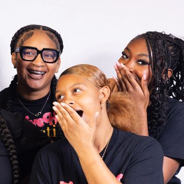 A joyful group of seven young women in matching shirts posing with smiles and playful gestures.