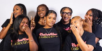 A group of six joyful women posing together in matching 'ThrivHer Collective' shirts.