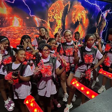 Group of kids in laser tag gear posing with peace signs in a fiery game arena.