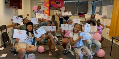 Group of people smiling and holding up cards in a decorated room with balloons.