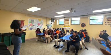 Teacher reading to students seated at desks in a classroom.