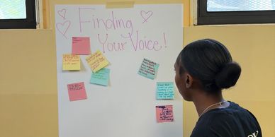 A person reads sticky notes on a board titled 'Finding Your Voice!'