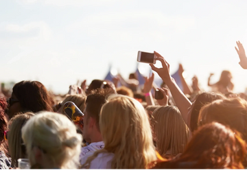 The back of a crowd of people with one holding up an iphone to take a photo 