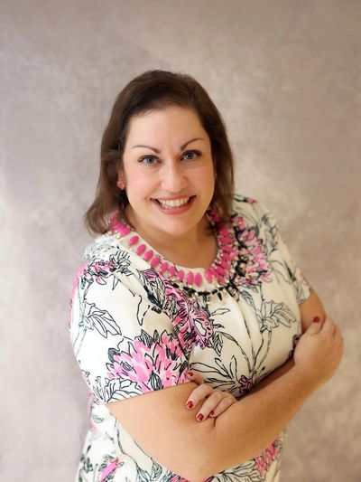 Smiling woman in floral dress with arms crossed.