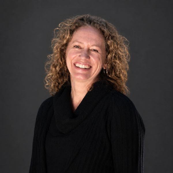 Woman with curly hair smiling in black sweater against dark background.