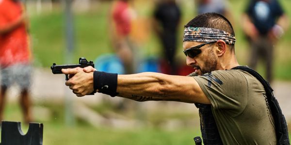 A man aiming a handgun during a shooting practice outdoors.
