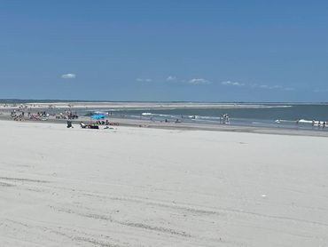 A sunny beach with people relaxing and swimming under a clear blue sky.