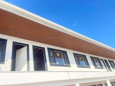 Newly constructed building with multiple black-framed windows and a wooden ceiling under clear blue sky.