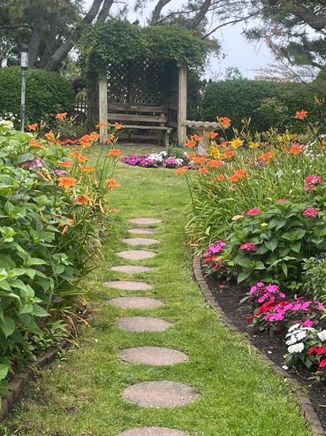A garden path with stepping stones leading to a wooden bench under a pergola.