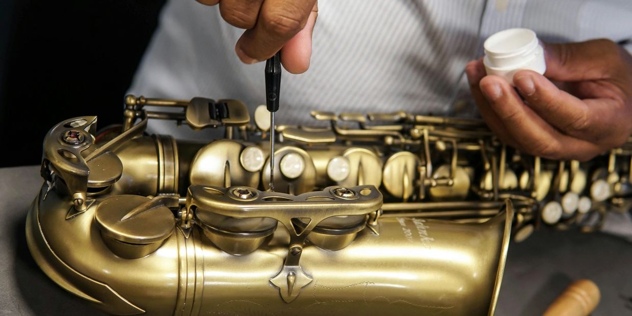 A band technician adjusting a valve on an alto saxophone.