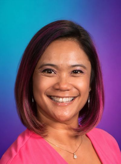 Smiling woman with pink hair highlights against a blue-purple background.