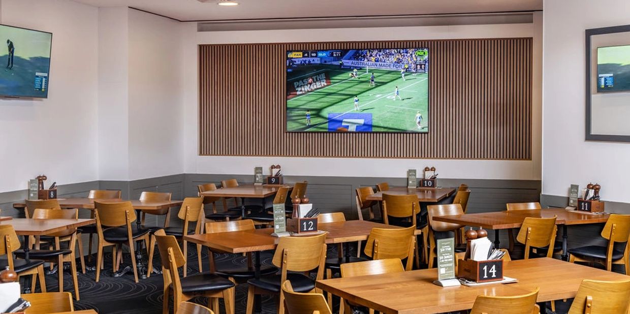 Empty dining area with wooden tables and chairs, TVs showing sports.