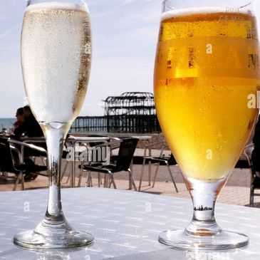 Two drinks, champagne and beer, on a table with a seaside view.