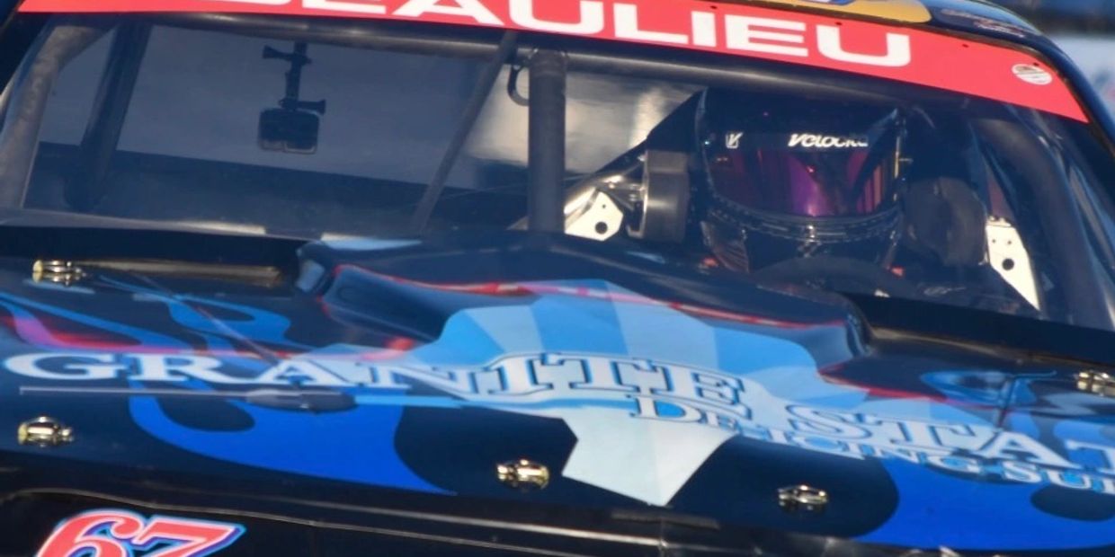 Close-up of a race car driver inside a black hooded race car.