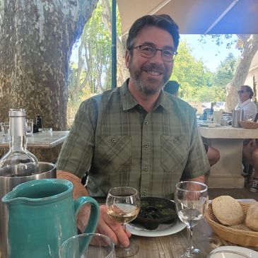 Man smiling at outdoor restaurant with food and drink.
