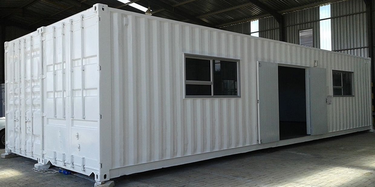 A white shipping container converted into a room with windows and a door.