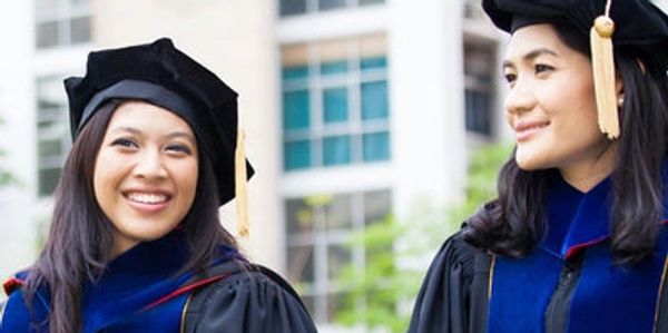 Two smiling graduates wearing academic gowns and caps.