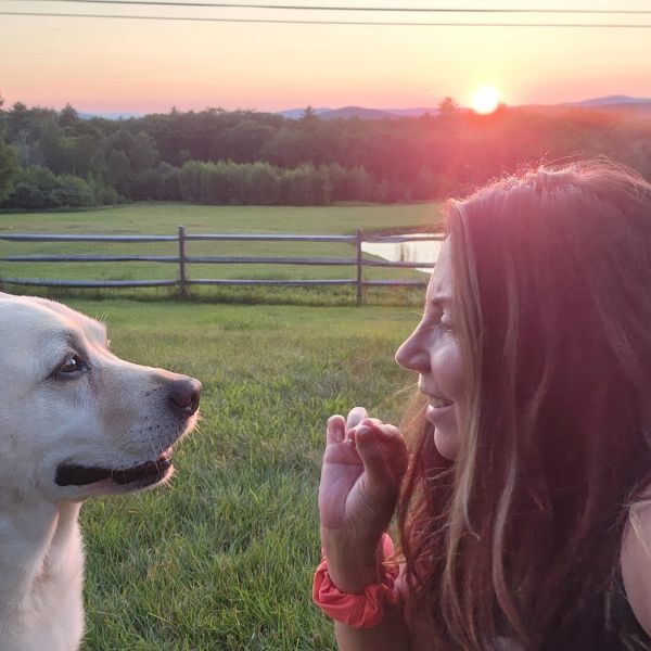 Woman and dog share a sunset moment outdoors.