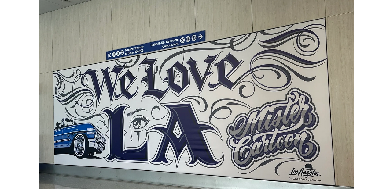 Mural saying 'We Love LA' with a classic car and eye art at an airport.