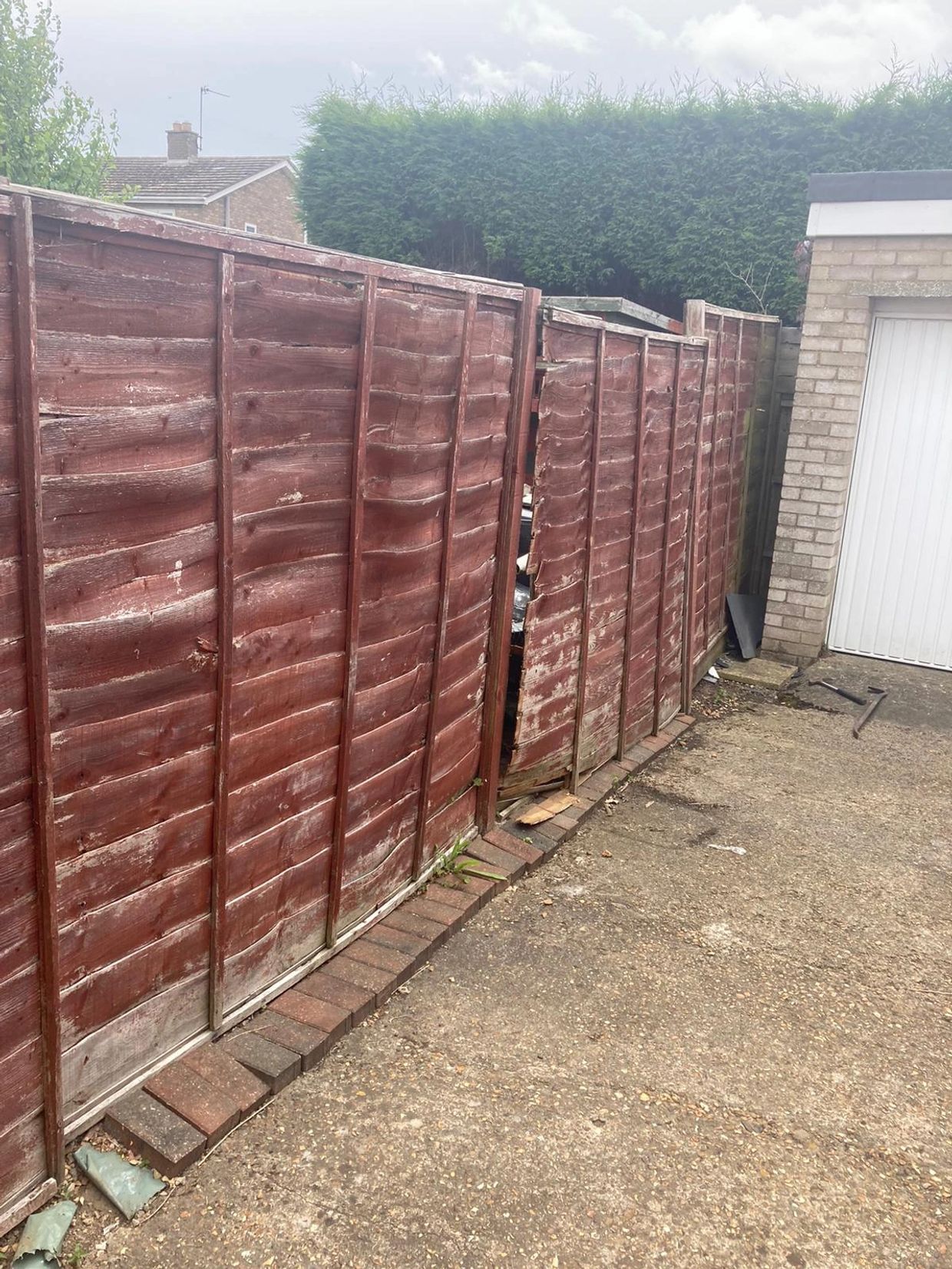 Warped wooden fence panels beside a driveway and garage.