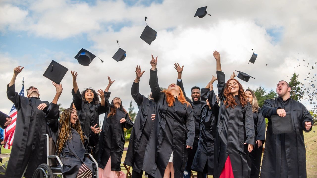 Graduates in black gowns joyfully tossing caps outdoors.