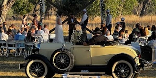 a bride and groom in the car and guest are watching 