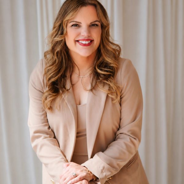 Smiling woman in beige blazer posing confidently.