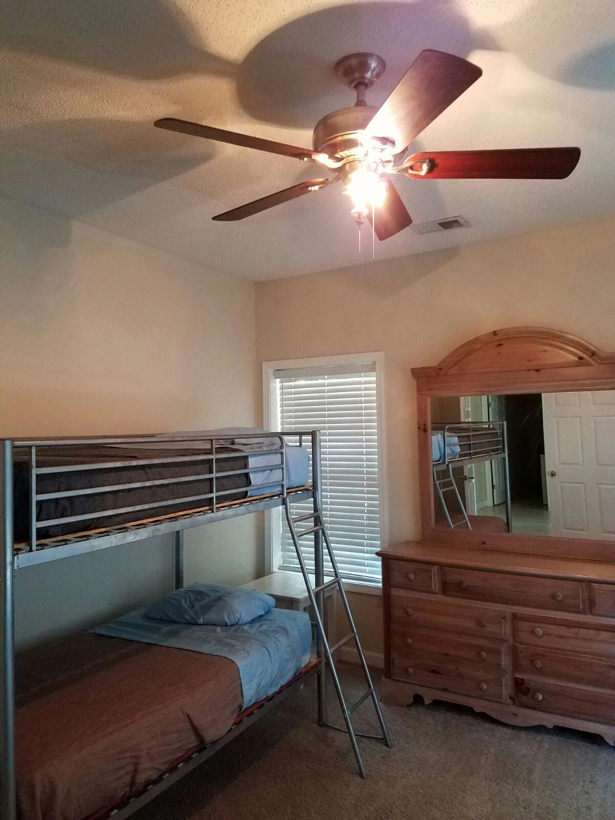 Cozy bedroom with metal bunk beds, wooden dresser, and ceiling fan.