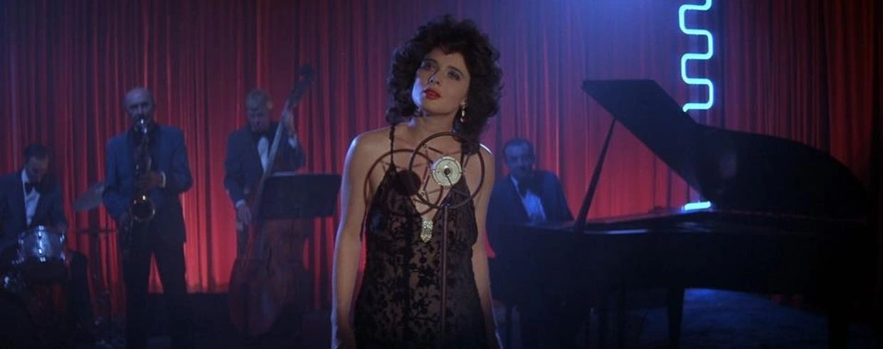 A woman sings in front of a jazz band with red curtains and blue neon lights.