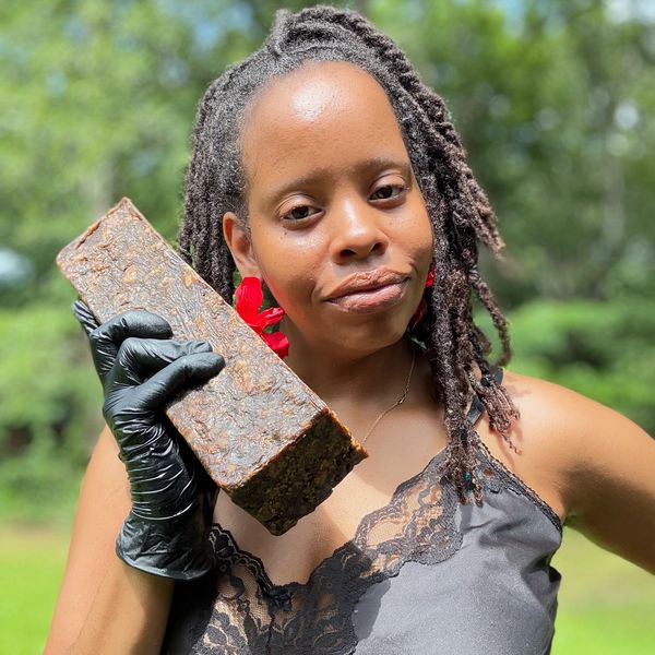 Woman holding a large brick-shaped object outdoors.