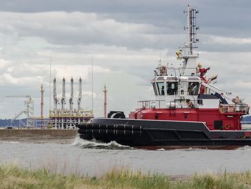 MARITIME TRANSPORT - Fireboat in the port channel on background of LNG terminal
