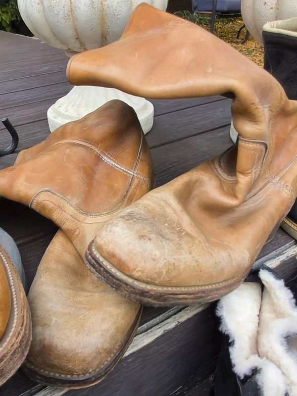 Worn-out brown leather boots on a wooden surface.