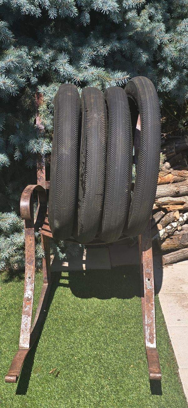 Four tires hanging on a rusty metal frame outdoors.