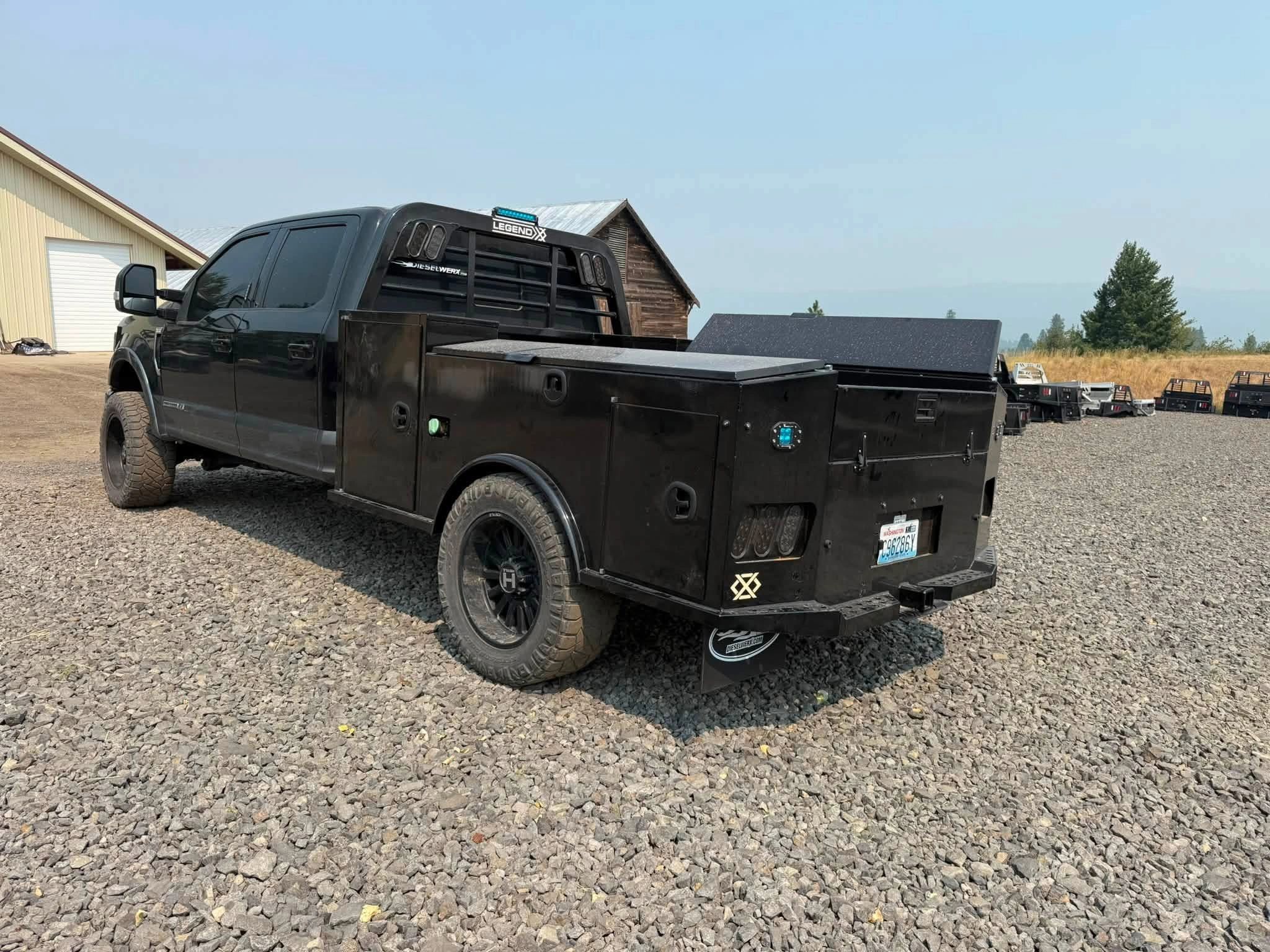 Black utility truck parked on gravel near a barn.