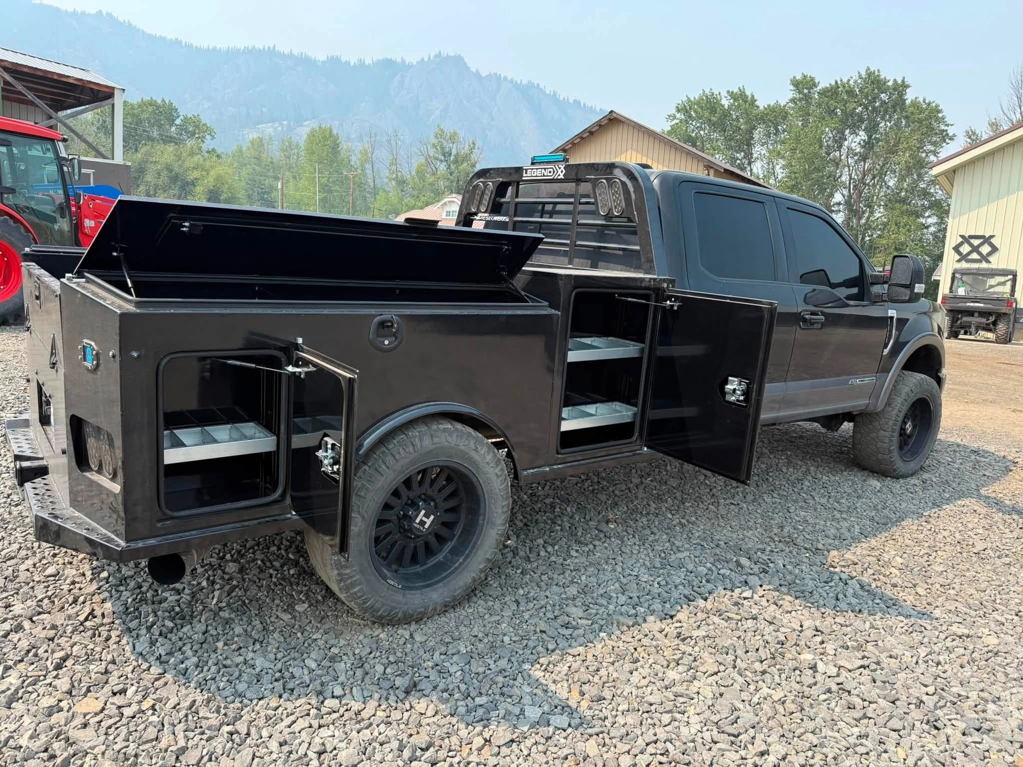 Black utility truck with open compartments on gravel.