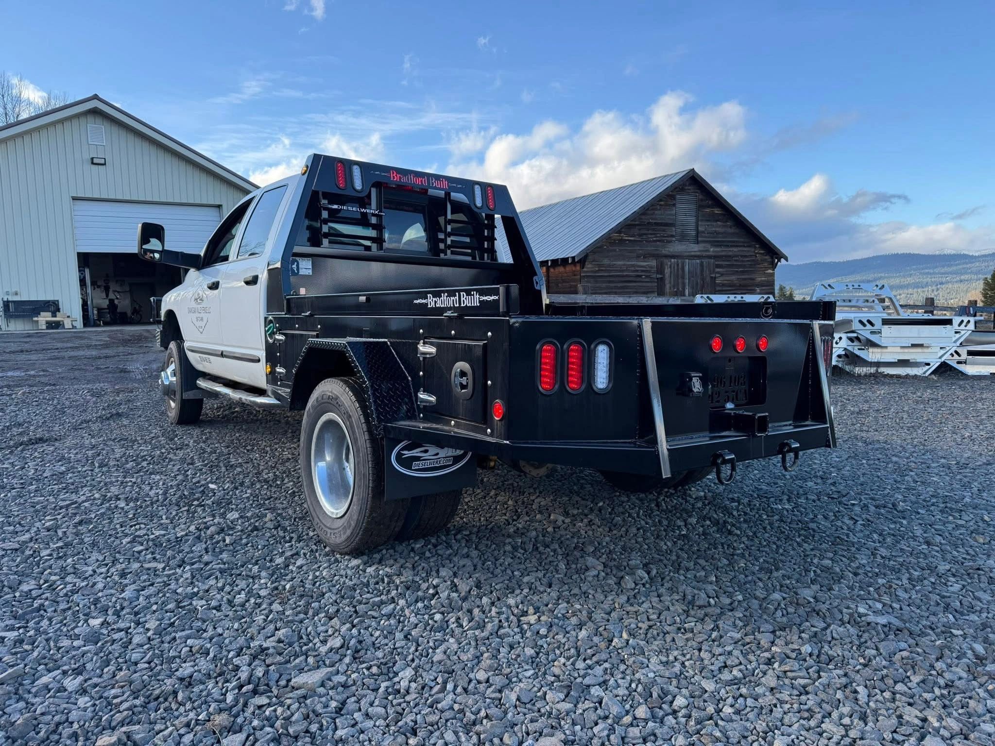 White truck with a black flatbed parked on gravel.