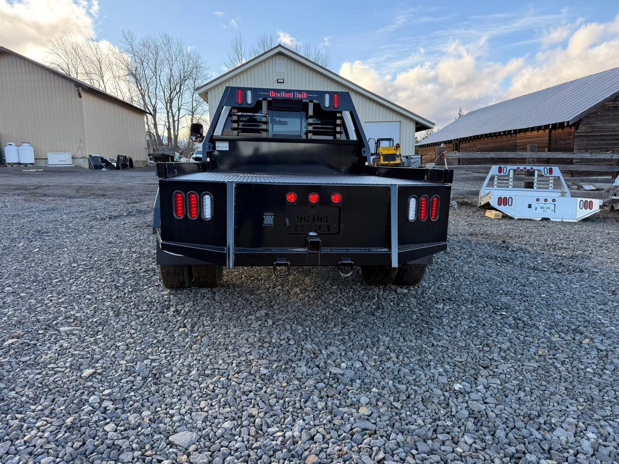 Rear view of a black flatbed truck on gravel.