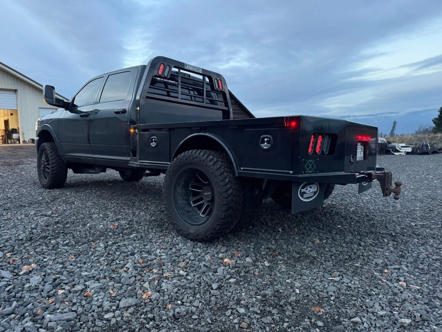 Black flatbed truck with rugged tires on gravel.