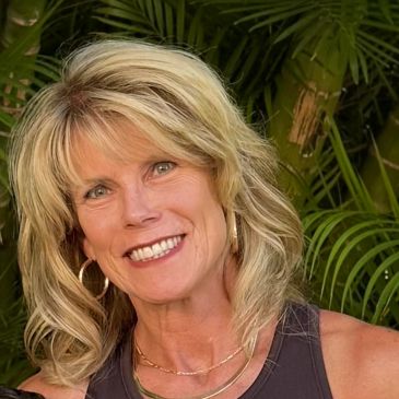 Smiling woman with blonde hair and hoop earrings outdoors.